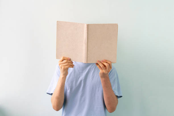 istock young man holding a book, reading and get knowledge standing near the wall, isolated 1302641511