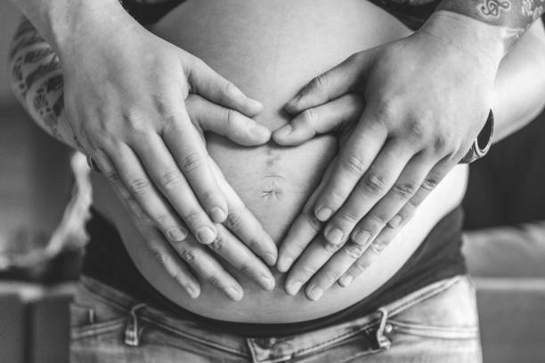 The hands of the future father rest on the hands of the future mother to form a heart on her belly