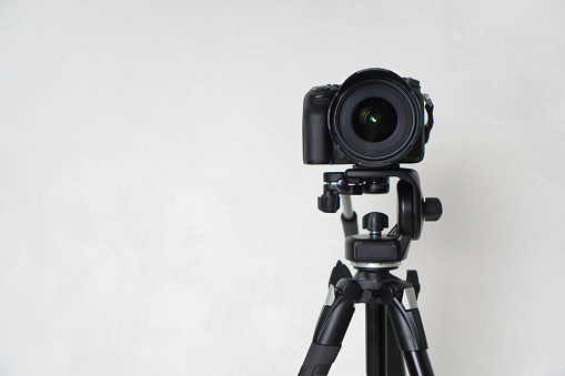 The camera standing on a tripod against the background of the wall in the room. The camera is looking at us. Background with copy space.