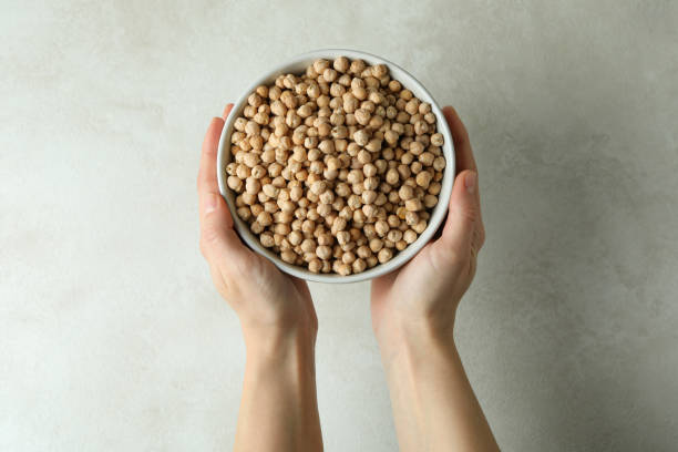 istock Female hands hold bowl of chickpea on white textured background 1302646520