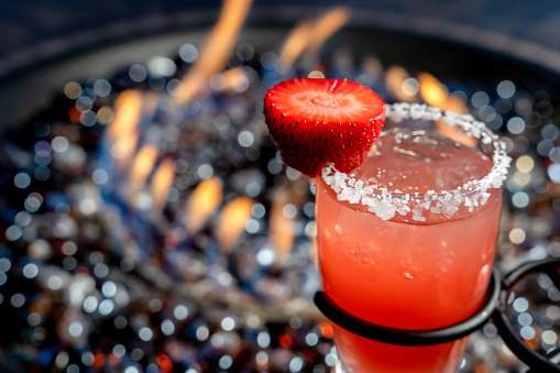 A Colorful Strawberry Margarita With The Glass Rimed With Salt And A Strawberry Garnish, A Propane Fire Pit In The Background