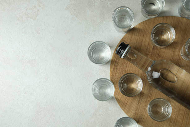 istock Board with bottle and shots of vodka on white textured background 1302649447