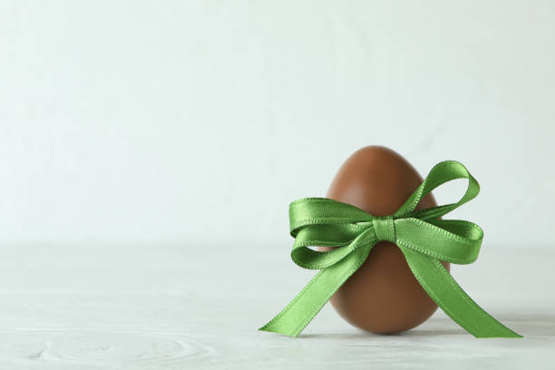 Easter chocolate egg with green ribbon on white wooden table