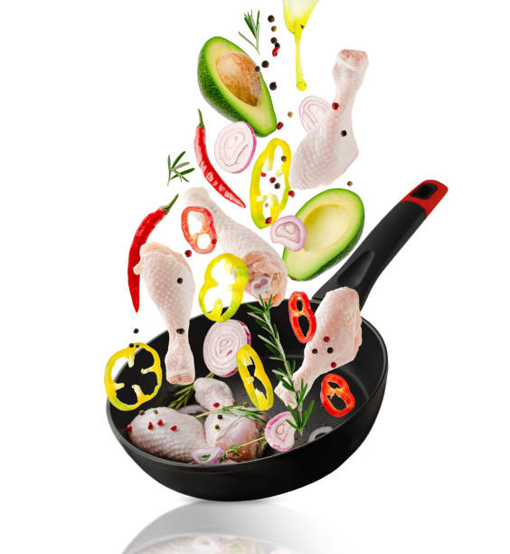 istock Raw chicken drumsticks and veggies ingredients falling into the frying pan. Isolated on white. Healthy eating 1302652078