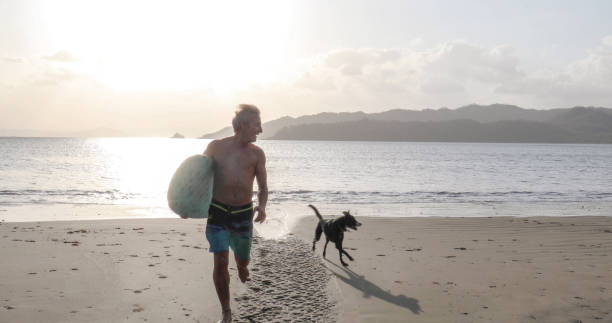 uomo e cane camminano lungo la spiaggia sabbiosa all'alba - men beach running shirtless foto e immagini stock