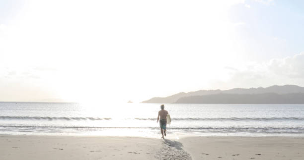 istock Man with boogie board runs down sandy beach at sunrise 1302652280