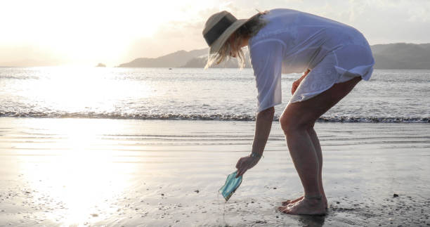 istock Woman picks up protective face mask littered on beach 1302652327