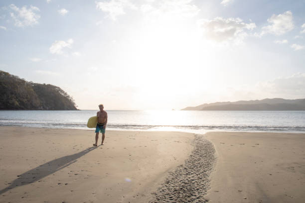 istock Man with boogie board walks down sandy beach at sunrise 1302652475