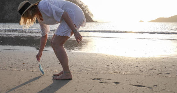 istock Woman picks up protective face mask littered on beach 1302652480