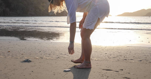 istock Woman picks up protective face mask littered on beach 1302652528
