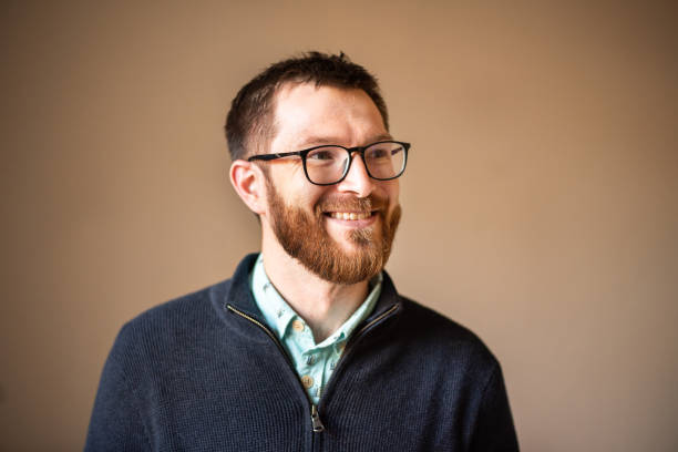 istock Smiling young man with glasses standing against a brown background 1302652596