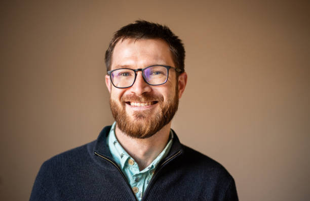 istock Young man with glasses smiling while standing against a brown background 1302652709