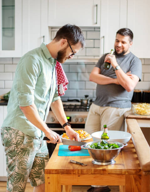 istock Two smiling friends talking over beers while making food in a kitchen 1302652952