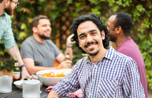 istock Young man smiling while sitting outside with friends in the background 1302652963