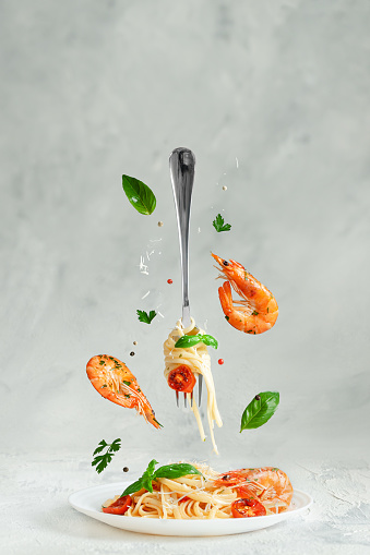 Pasta linguine with prawns and fork flying over the dish. Creative still life. Italian food concept