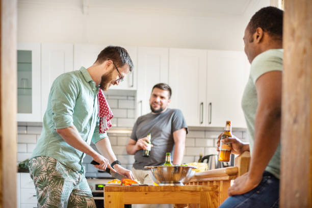 istock Group of smiling friends talking over beers while making food in a kitchen 1302653537