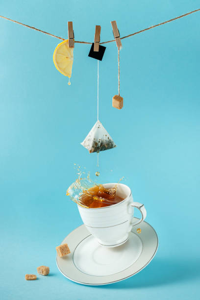 istock Tea bag, lemon and sugar hanging on the rope over splashing tea on blue background. Creative still life concept. 1302653583