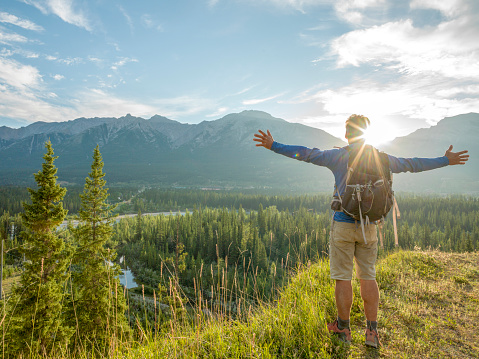 Hiker stretches arms out on mountain bluff, sunrise