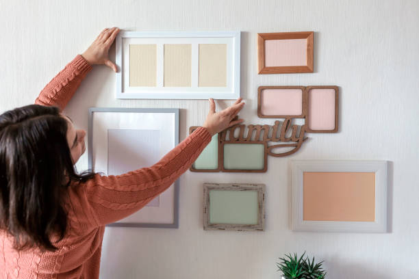 istock Girl hanging frame on white wall with set of different empty vertical and horizontal picture frames 1302658372