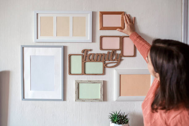 istock Girl hanging frame on white wall with set of different empty vertical and horizontal picture frames 1302658452