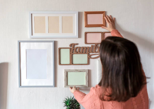 istock Girl hanging frame on white wall with set of different empty vertical and horizontal picture frames 1302658472
