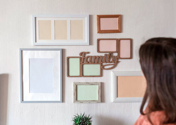 istock Girl hanging frame on white wall with set of different empty vertical and horizontal picture frames 1302658496