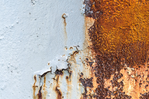 An old pitted and weathered rusty metal sheet background framed by old rusty bolts. Lots of texture with subtle abstract colors of the patina.