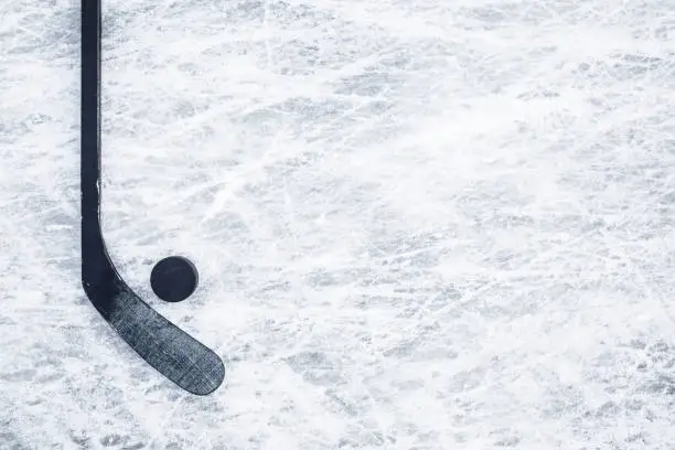 Photo of Black hockey stick and rubber puck on ice background. Closeup. Empty place for text. Top down view.