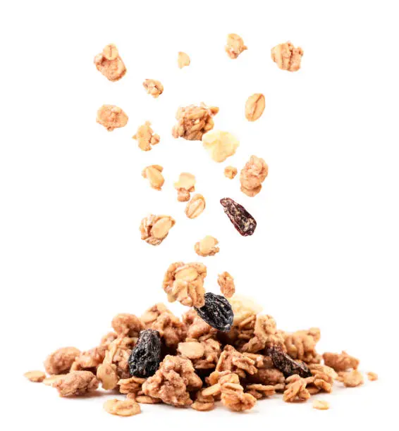 Photo of Crispy granola with raisins and banana falling on a heap on a white background. Isolated
