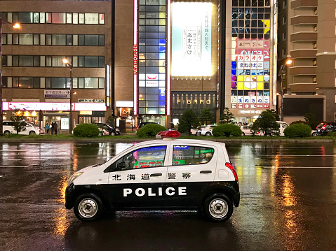 Sapporo - Japan - September 23, 2019: A small Police Car at street in a raining night, on back, lighting billboard ads.