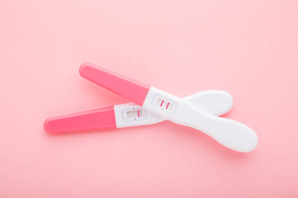 istock Pregnancy tests with one stripe and two stripes on light pink table background. Pastel color. Negative and positive result. Closeup. Top down view. 1302667769