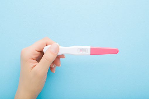 Mujer adulta joven sosteniendo a mano la prueba de embarazo con una raya sobre fondo de mesa azul claro. Color pastel. Resultado negativo. Closeup. Vista de arriba hacia abajo. photo