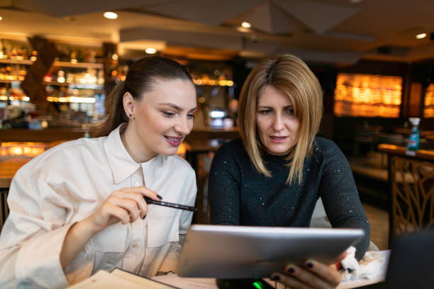 istock Two businesswoman sitting in cafe and talking about project while looking at digital tablet 1302670554