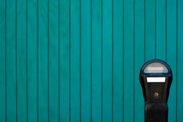 On-street blank parking meter in front of a teal wooden background