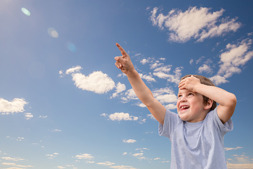 Little happy child boy looking up at sky and points up with his finger