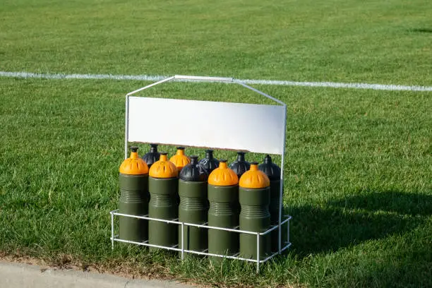 Photo of Sport bottles of fresh water or energy drink on soccer, football field/