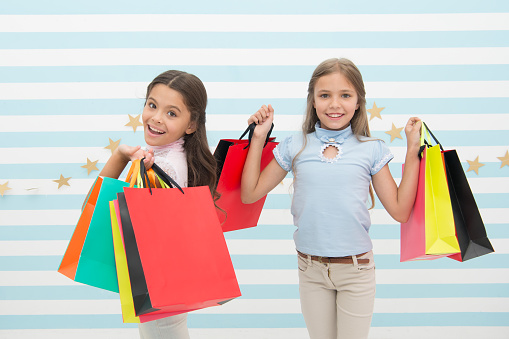 Children satisfied shopping striped background. Obsessed with shopping and clothing malls. Discount concept. Kids cute girls hold shopping bags. Shopping discount season. Spending great time together.