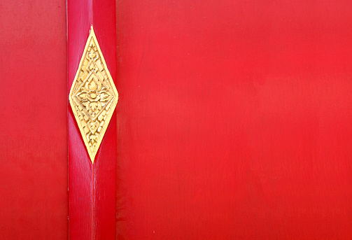 Red door with metallic element in asian style. Red wooden gate with golden details. Door with thai floral ornament.