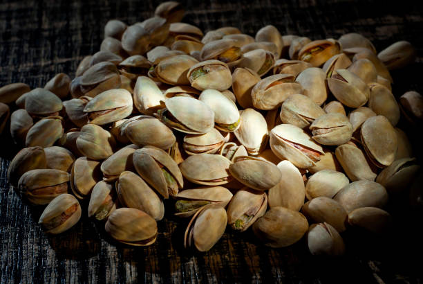 istock Pistachio texture close up. Nuts on a pile on a black wooden board. Contrasting dramatic light as an artistic effect. 1302683467