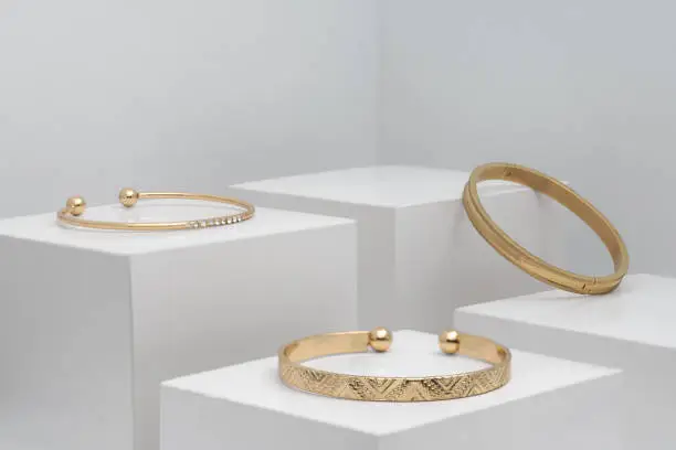 Photo of Three modern golden bracelets on white boxes with copy space
