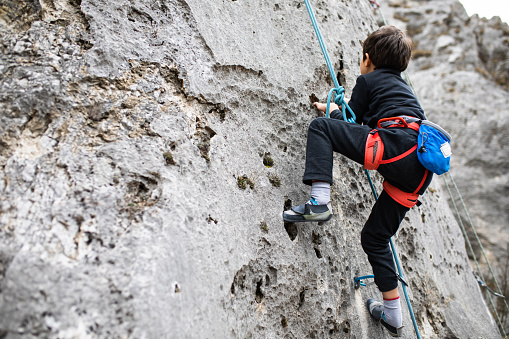 A young boy rock climber is climbing a huge natural rock formation