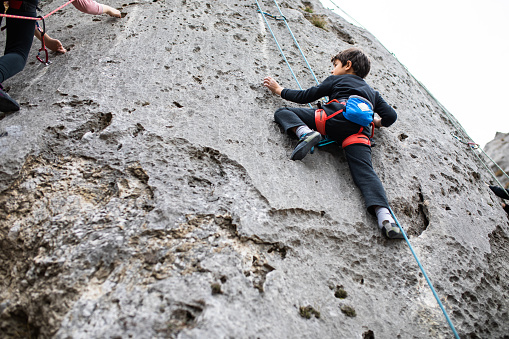 A young boy rock climber is climbing a huge natural rock formation and looking at a young girl climbing next to him