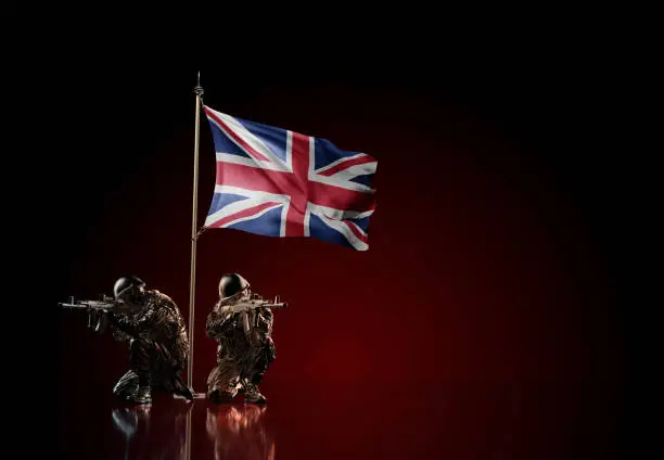 Concept of military conflict with soldier statues and waving national flag of United Kingdom. Illustration of coup idea. Two guards defending the symbol of country against red wall
