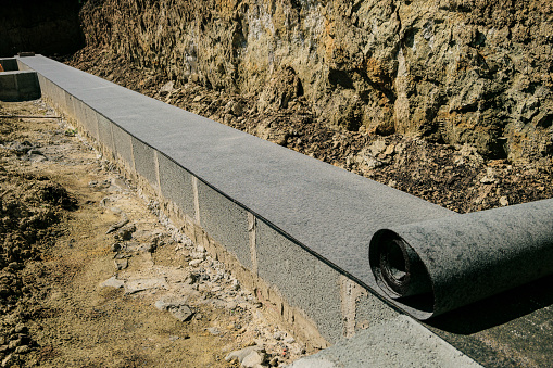 Long line of rolled bitumen waterproofing material in two layers lies on the masonry of concrete blocks. Horizontal waterproofing the basement of a house under construction.