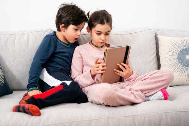 istock Two mixed-race kids sitting on sofa with tablet 1302699424