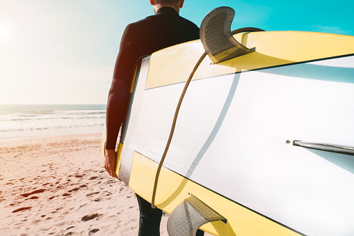 Surfer in wetsuit holding yellow surfboard on the beach near the ocean. High quality photo