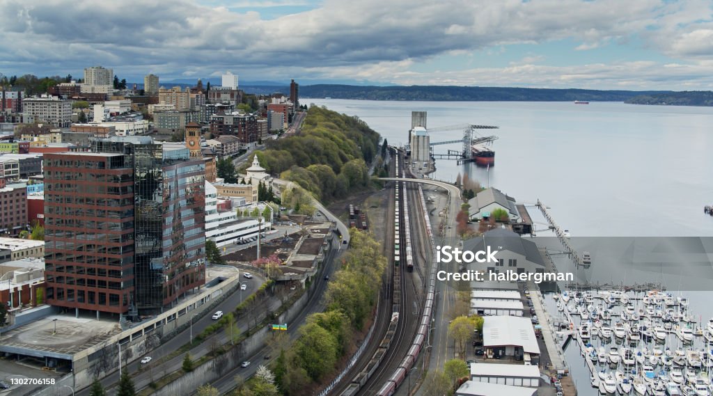 Freight Train Passing Between Downtown Tacoma and Commencement Bay Drone shot of Tacoma, Washington on a cloudy day. Overcast Stock Photo