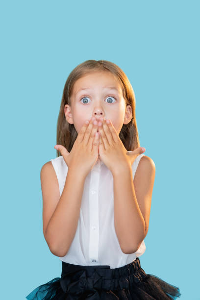 shocked kid back to school surprised little girl Shocked kid. Back to school. Unexpected news. Portrait of surprised overwhelmed cute little girl in formal outfit covering mouth with hands isolated on blue background. white shirt black skirt stock pictures, royalty-free photos & images