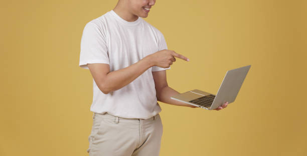 istock happy glad rejoicing cheerful young asian man holding pointing finger at laptop computer screen isolated on yellow background 1302708366