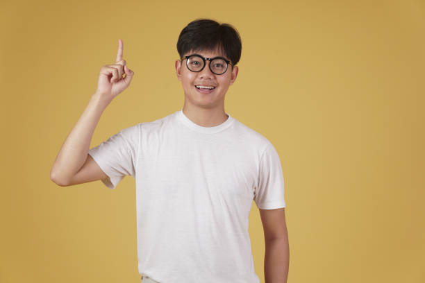 istock happy cheerful young asian man student dressed casually wearing eyeglasses pointing finger up having idea isolated on yellow background 1302708367